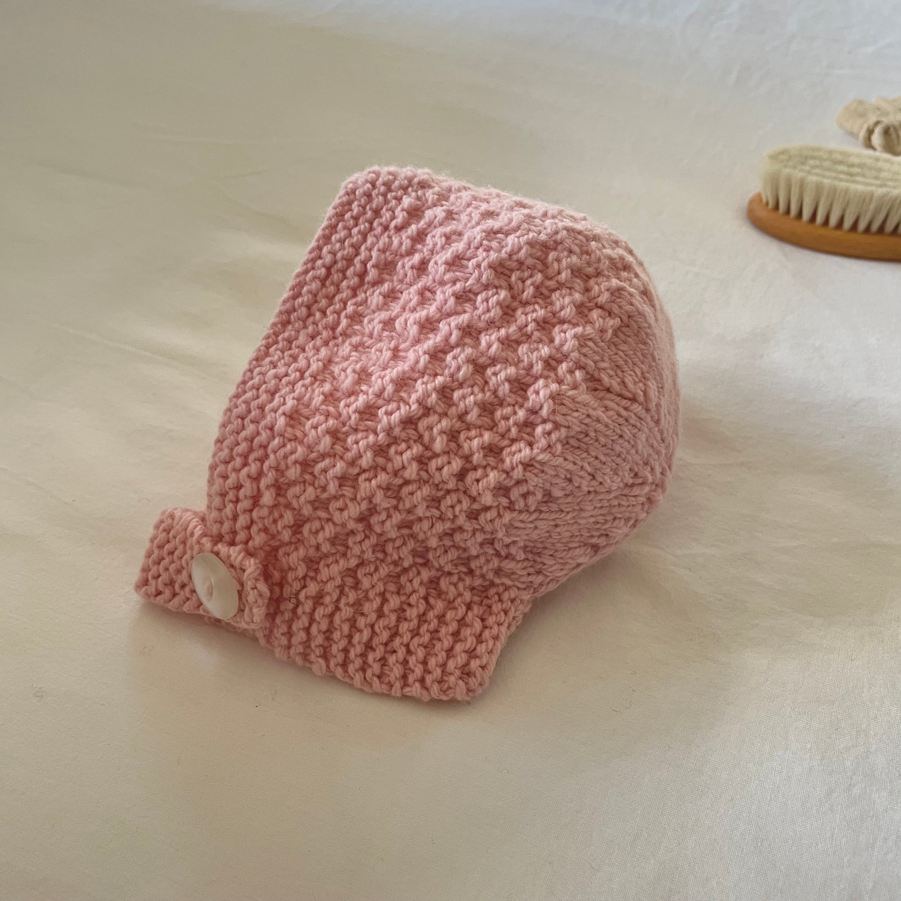 Pink knitted baby hat on a light surface
