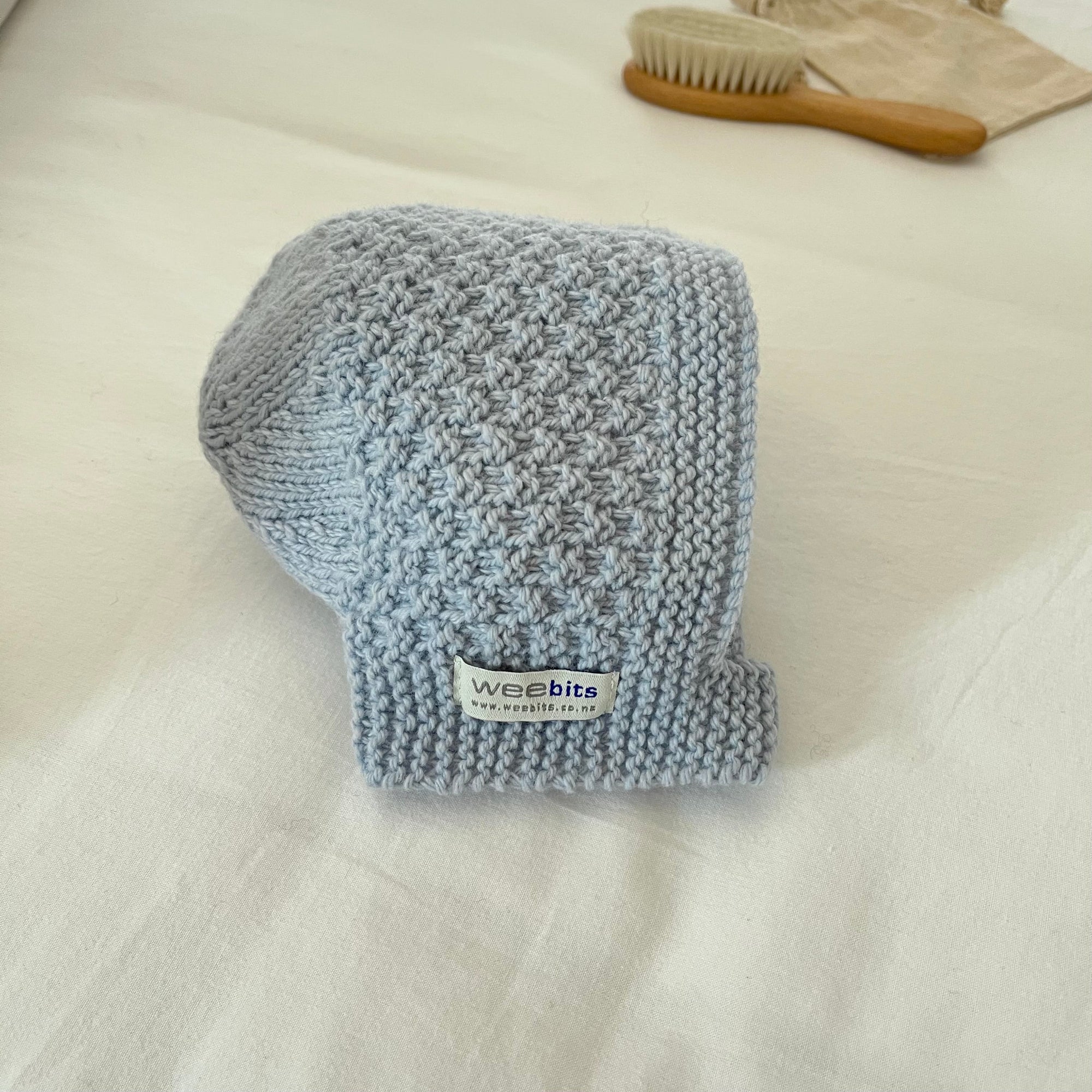 Knitted blue baby bootie with 'weebits' label on a white surface