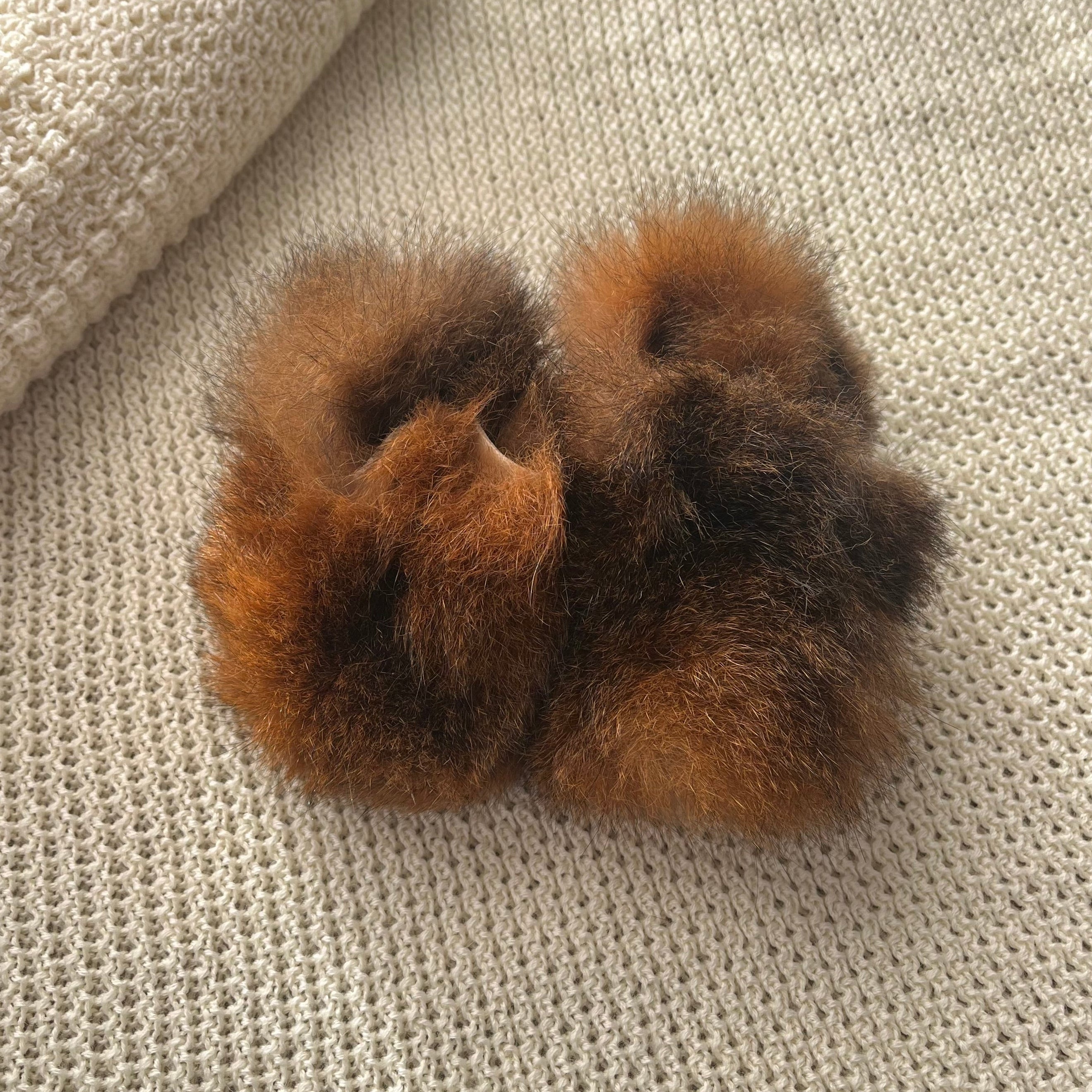 Pair of brown fuzzy possum booties on a textured beige surface