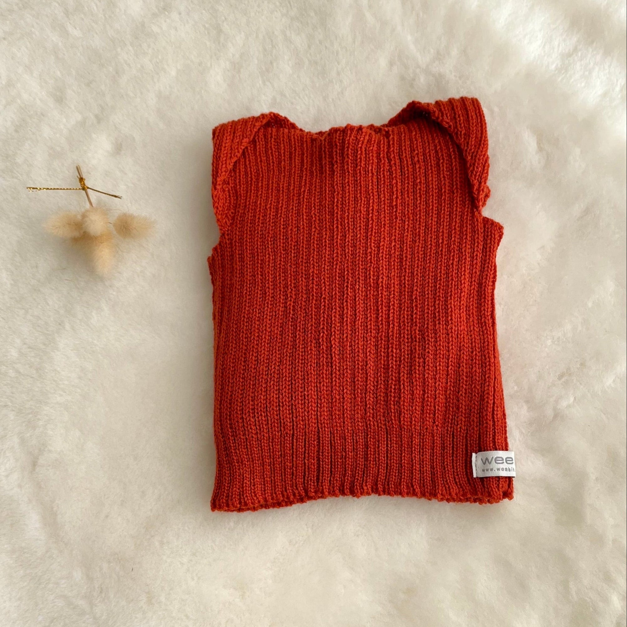 Burnt orange premature baby vest on sheepskin rug