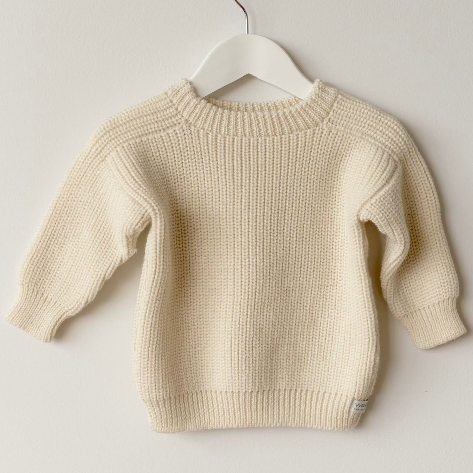 natural sweater on a white hanger against a light gray background