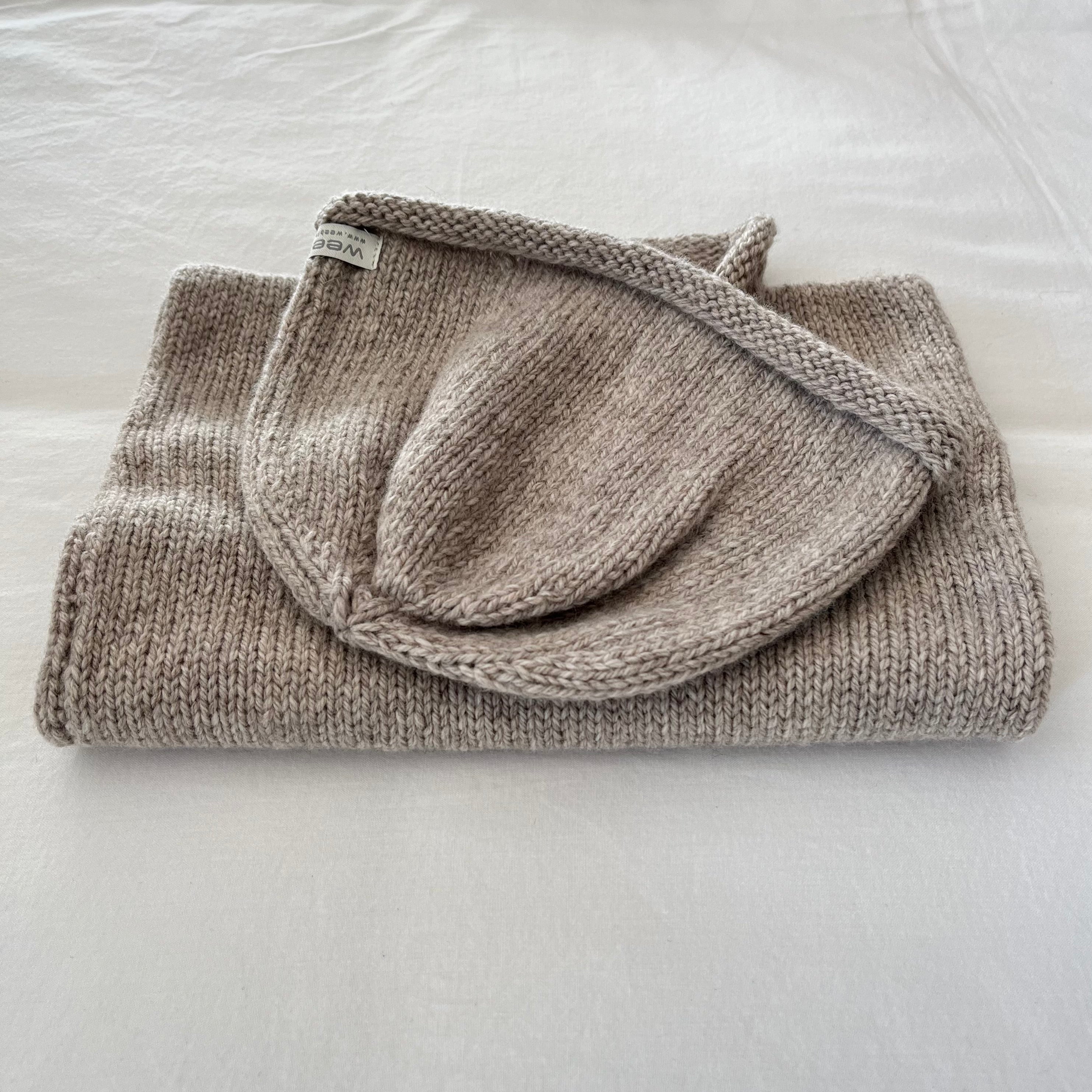 Folded oatmeal marle knitted vest and beanie on a light gray surface