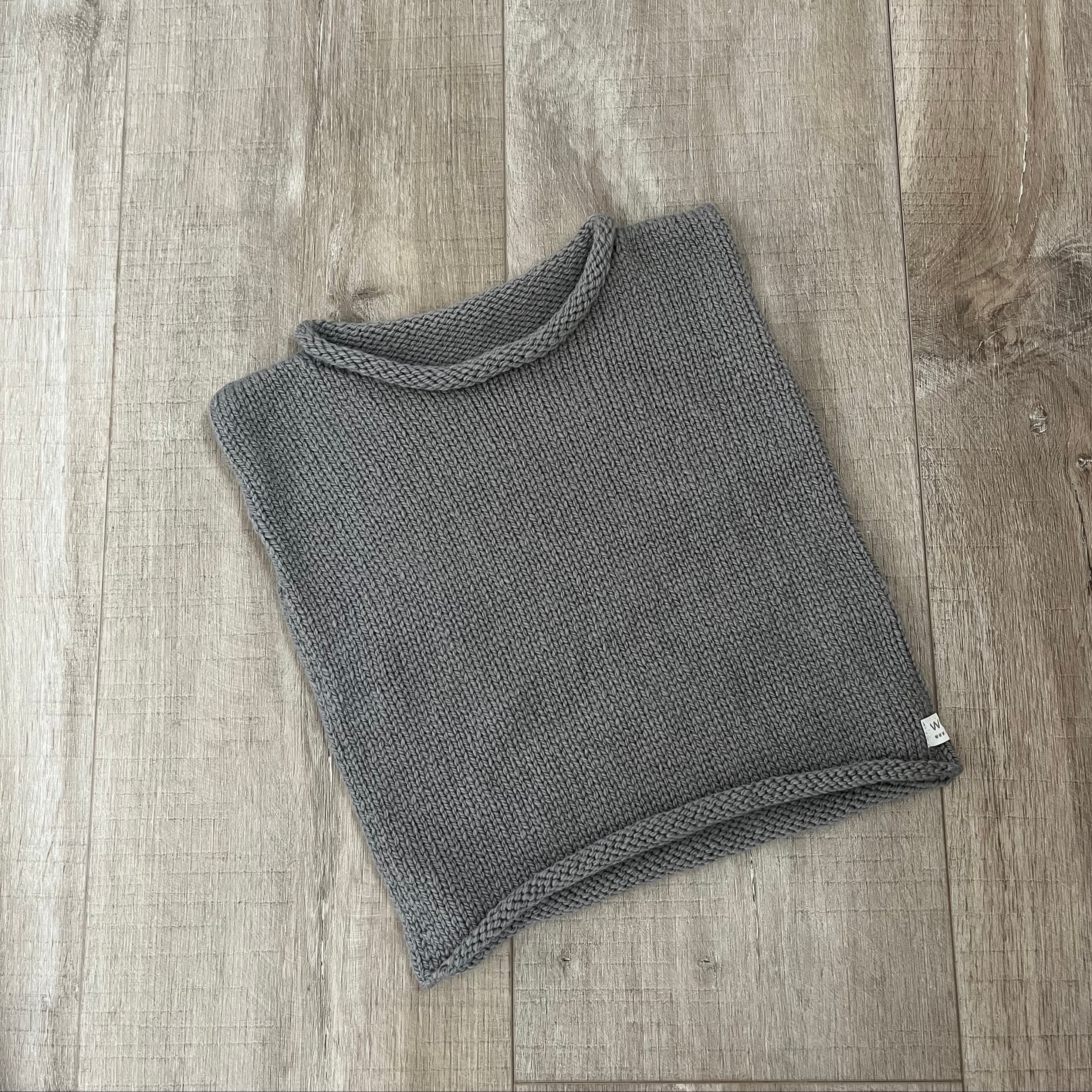 A mushroom knit vest  placed on a light brown wood surface.