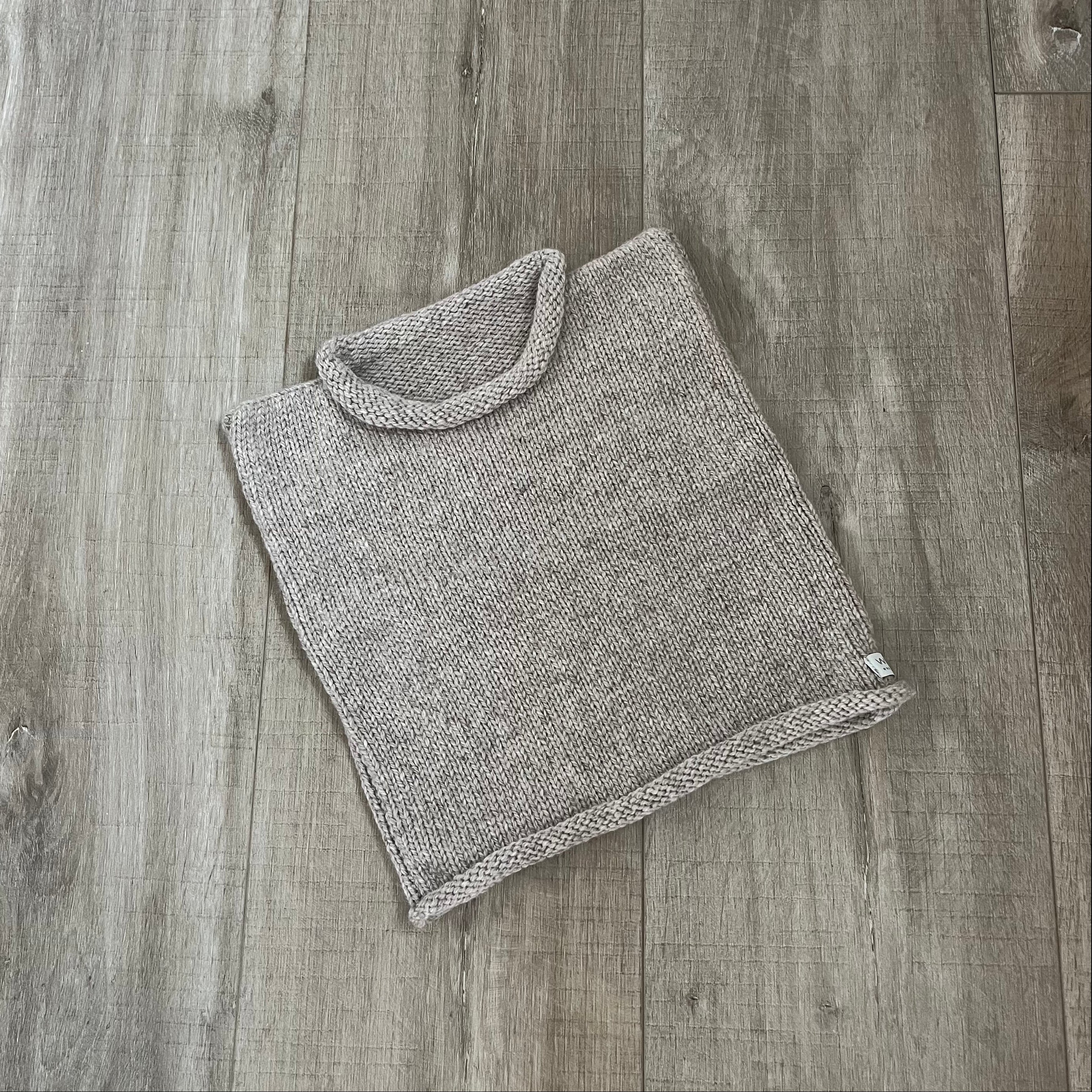 A Oatmeal knit vest  placed on a light brown wood surface.