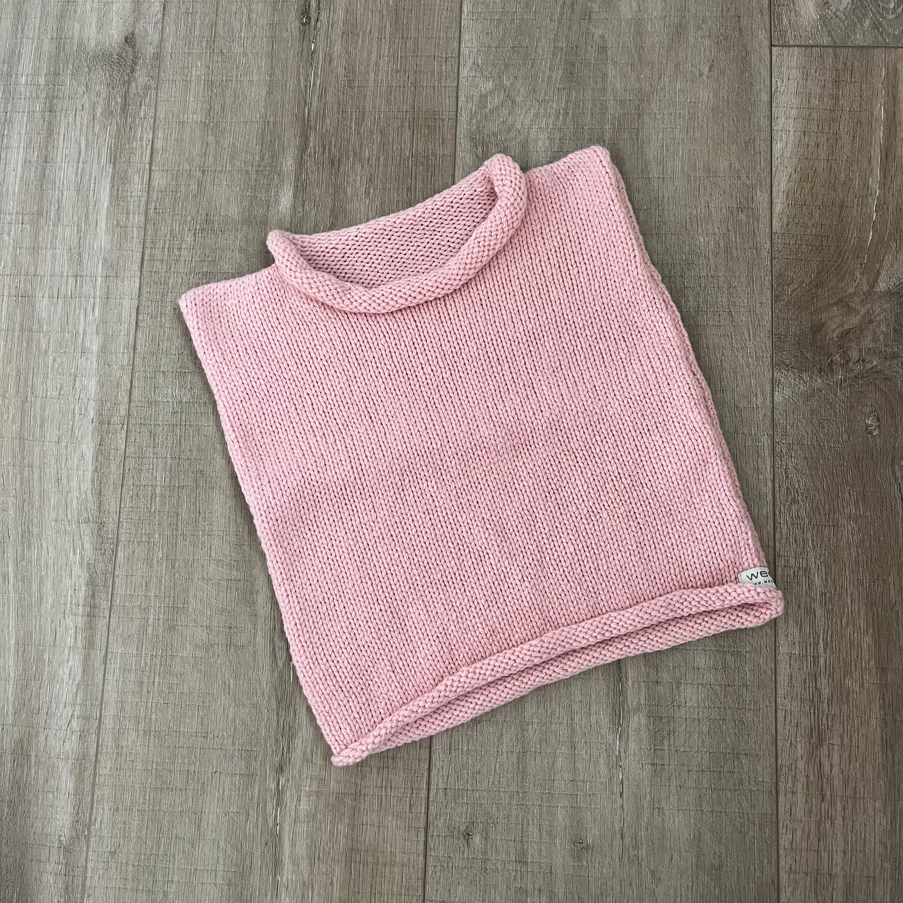 A pink knit vest  placed on a light brown wood surface.