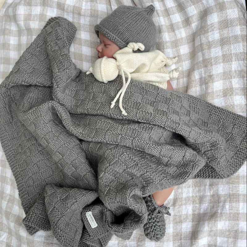 Sleeping baby in mushroom travel rug, beanie and booties on gingham blanket