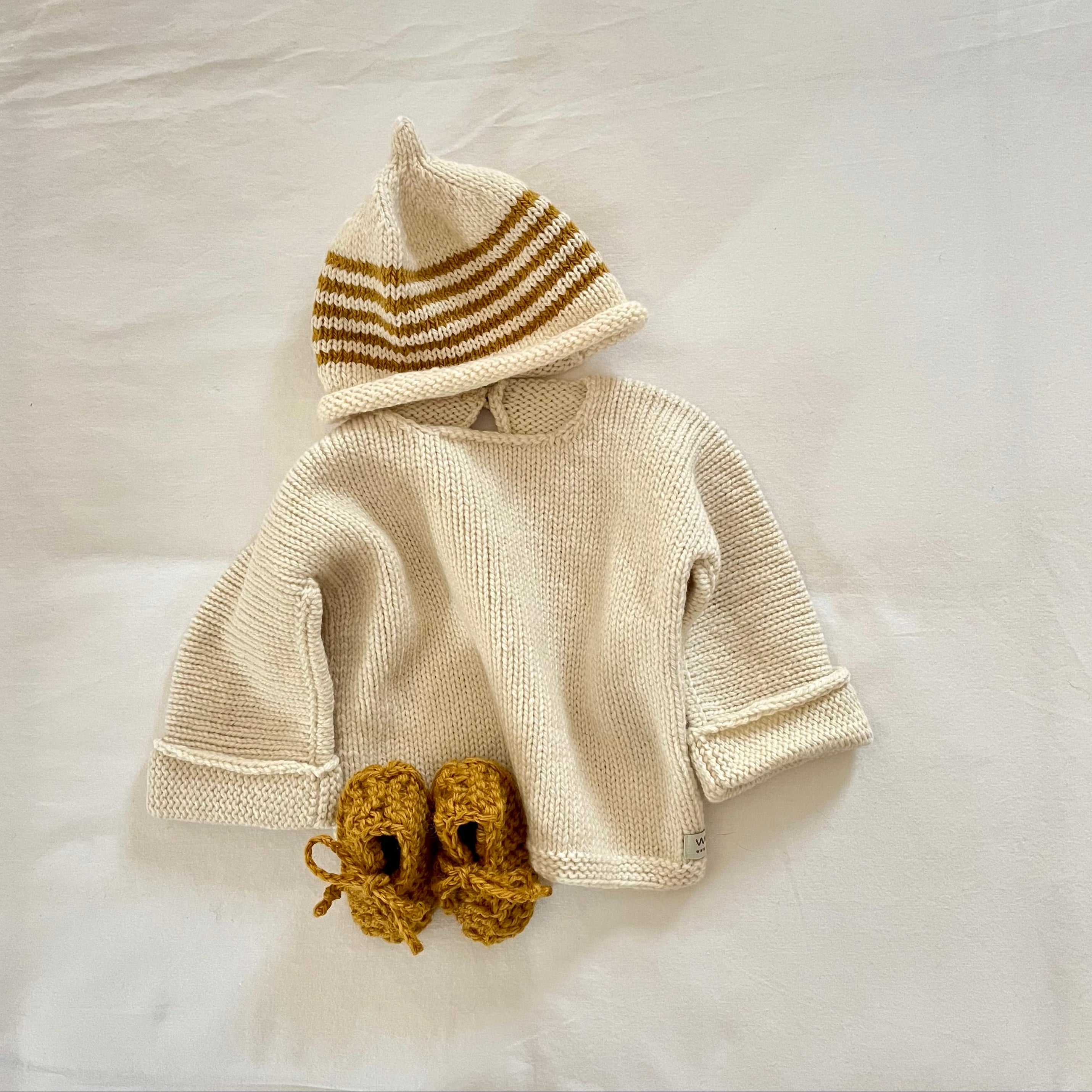 Knitted baby sweater with beanie and matching booties on a light background