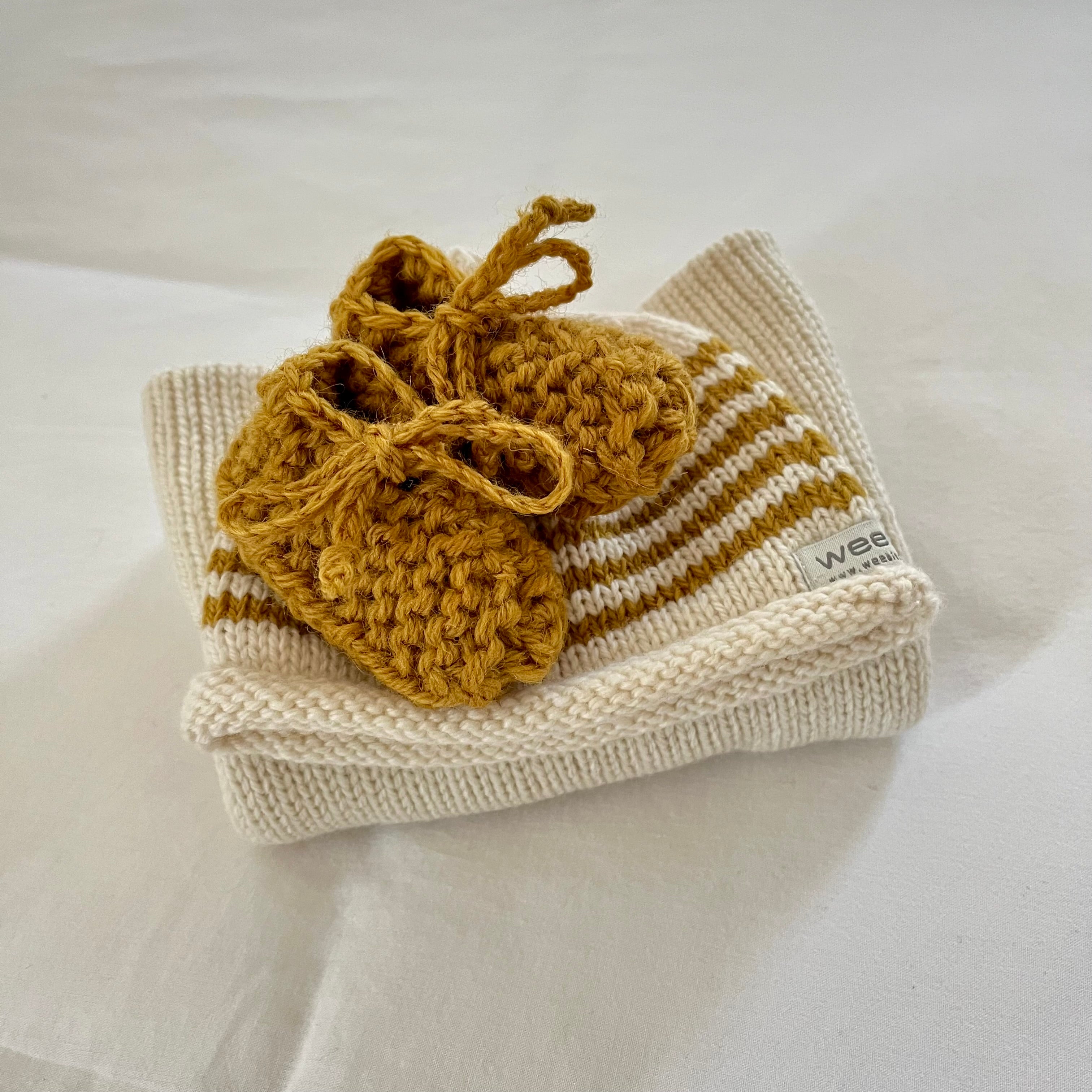 Knitted baby sweater booties and hat set on a light background