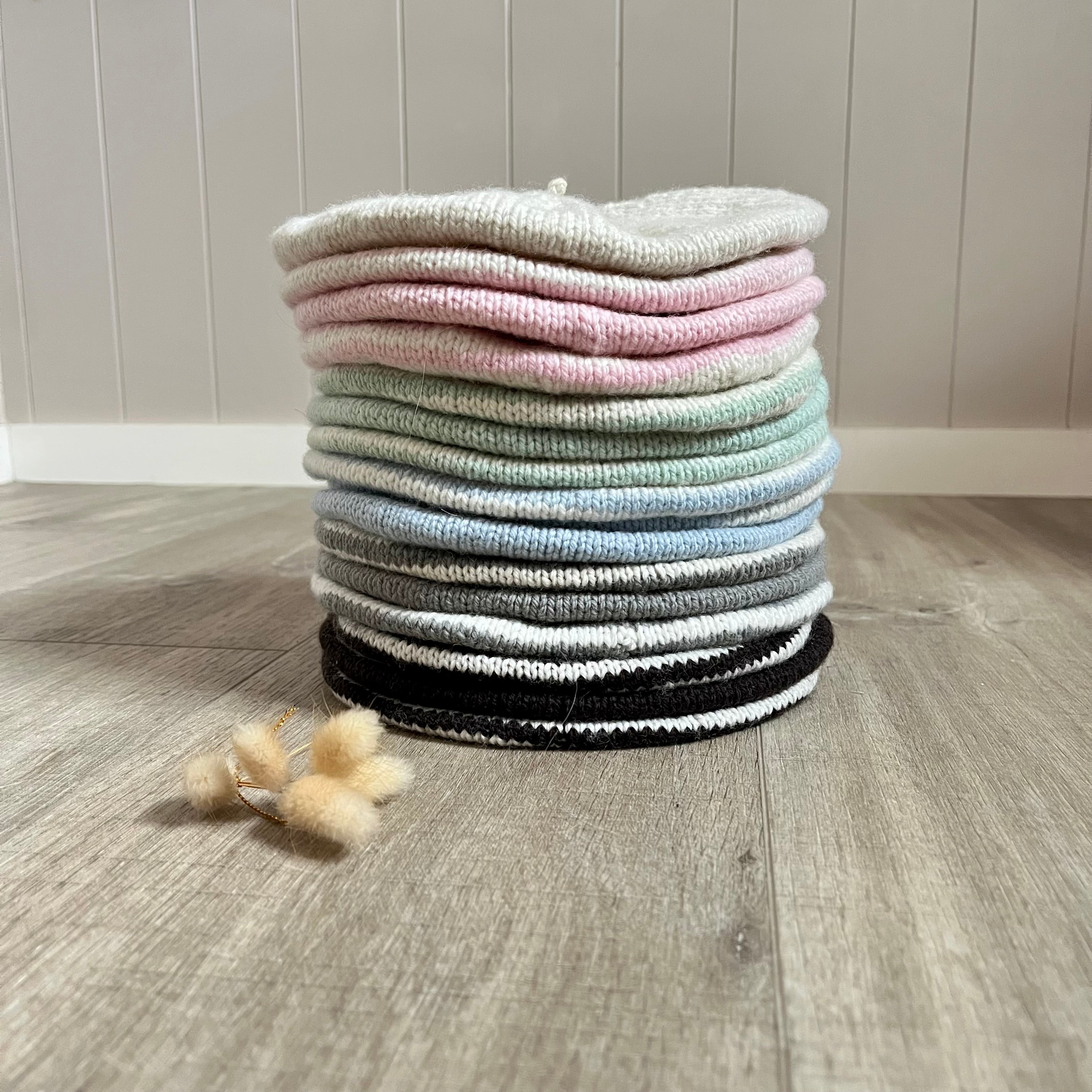 Stack of colorful berets on a wooden floor with a neutral background