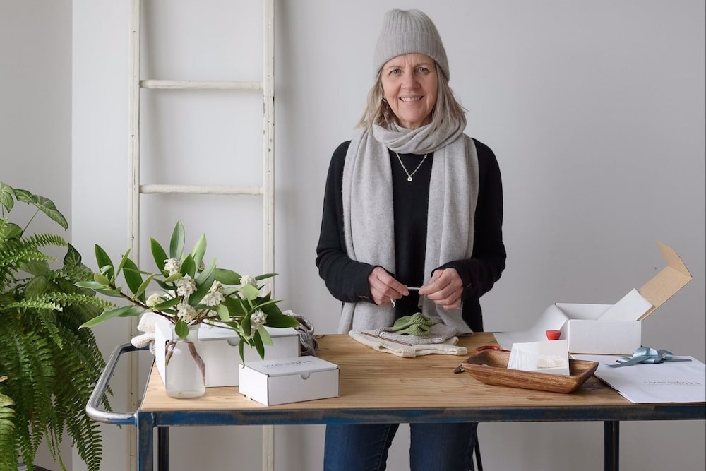 Woman standing behind a table with plants and Weebits boxes in a room with a ladder and white wall.