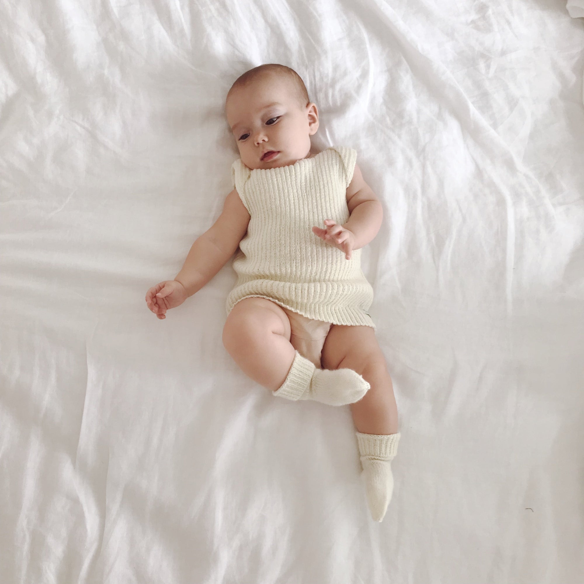 Baby wearing merino singlet vest and socks laying down